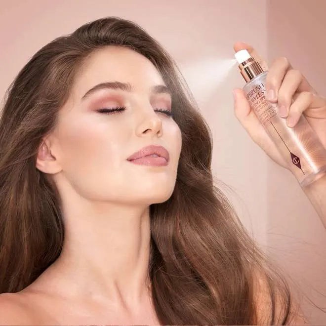Charlotte Tilbury setting spray bottle next to makeup brushes and cosmetic products, emphasizing its role in a complete makeup routine