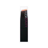 Huda Beauty foundation stick 315B Shortcake next to other makeup products for comparison