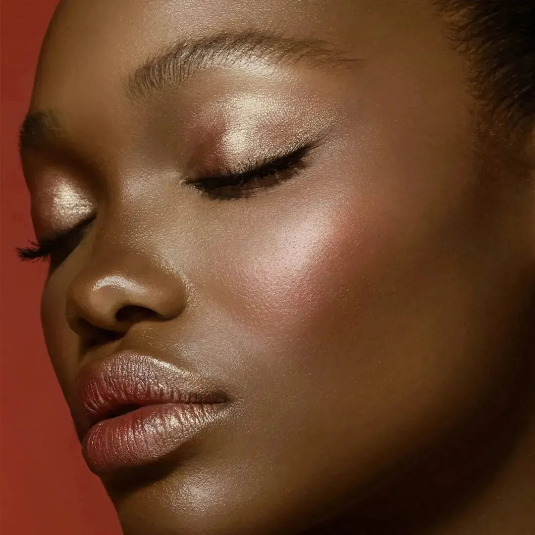 A model wearing makeup achieved using the Natasha Denona Bloom Face Glow Palette, showcasing a radiant complexion with rosy cheeks, illuminated cheekbones, and possibly shimmering eyelids or lips, demonstrating its multi-use capabilities.